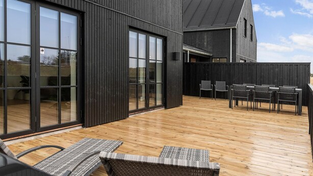 A modern building with large glass doors and a wooden deck with outdoor furniture. - 3 bedroom nice home in Løkken (Løkken)