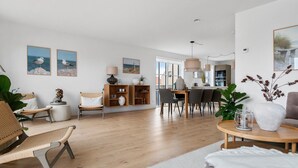 A spacious living room with a wooden floor, a dining area with a table and chairs, and a kitchen in the background. - 3 bedroom nice home in Løkken (Løkken)