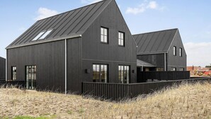A modern two-story building with a dark exterior, large windows, and a sloped roof. - 3 bedroom nice home in Løkken (Løkken)