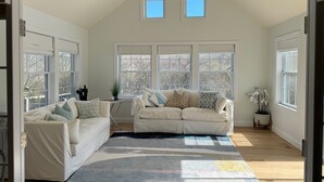 A spacious living room with two white sofas, a colorful rug, and large windows providing natural light. - Perfect Retreat for Families - Close to Amazing Wineries, Beaches, and Dining! (Southold)