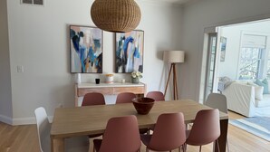 A modern dining area with a wooden table, pink chairs, abstract art on the wall, and a floor lamp. - Perfect Retreat for Families - Close to Amazing Wineries, Beaches, and Dining! (Southold)