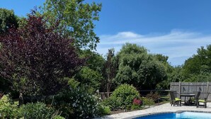 A curved swimming pool with a stone deck and a metal ladder. - Perfect Retreat for Families - Close to Amazing Wineries, Beaches, and Dining! (Southold)