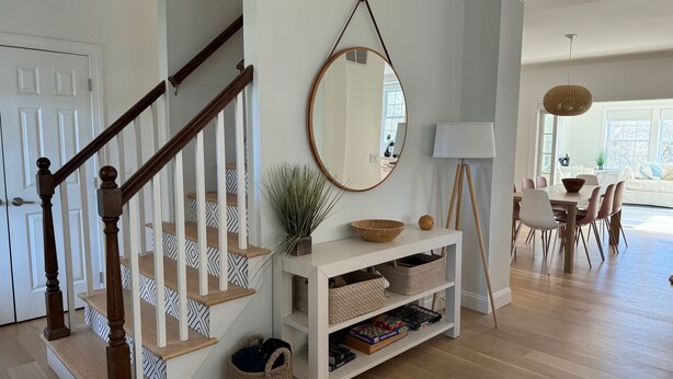 A staircase with wooden balusters, a white console table with baskets, a round mirror, and a dining area with a table and chairs. - Perfect Retreat for Families - Close to Amazing Wineries, Beaches, and Dining! (Southold)