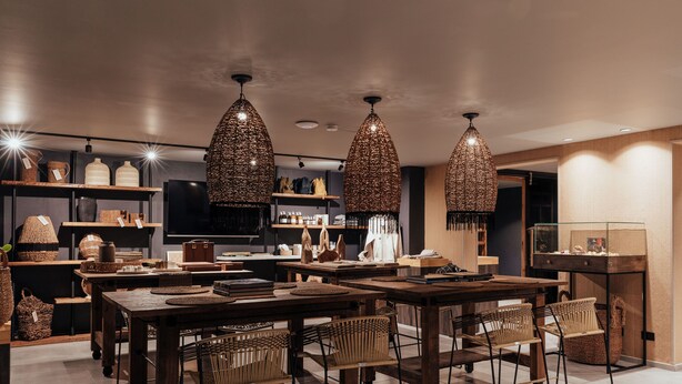 A modern dining area with wooden tables and chairs, hanging woven light fixtures, and shelves with various items. - Sui Posada Boutique (Medellín)