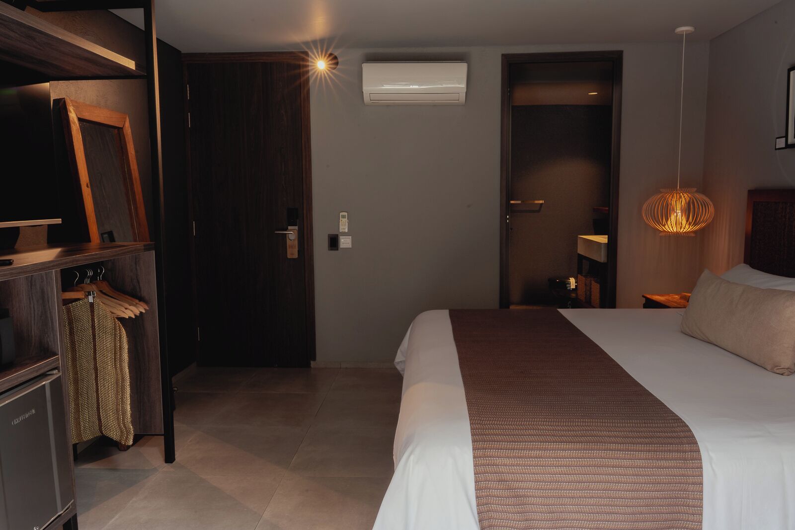 Habitación de hotel con cama, armario, lámpara colgante y equipo de aire acondicionado.