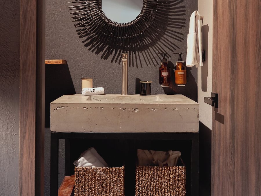 Un baño con un espejo redondo, un lavabo y dos cestas de mimbre en un estante.