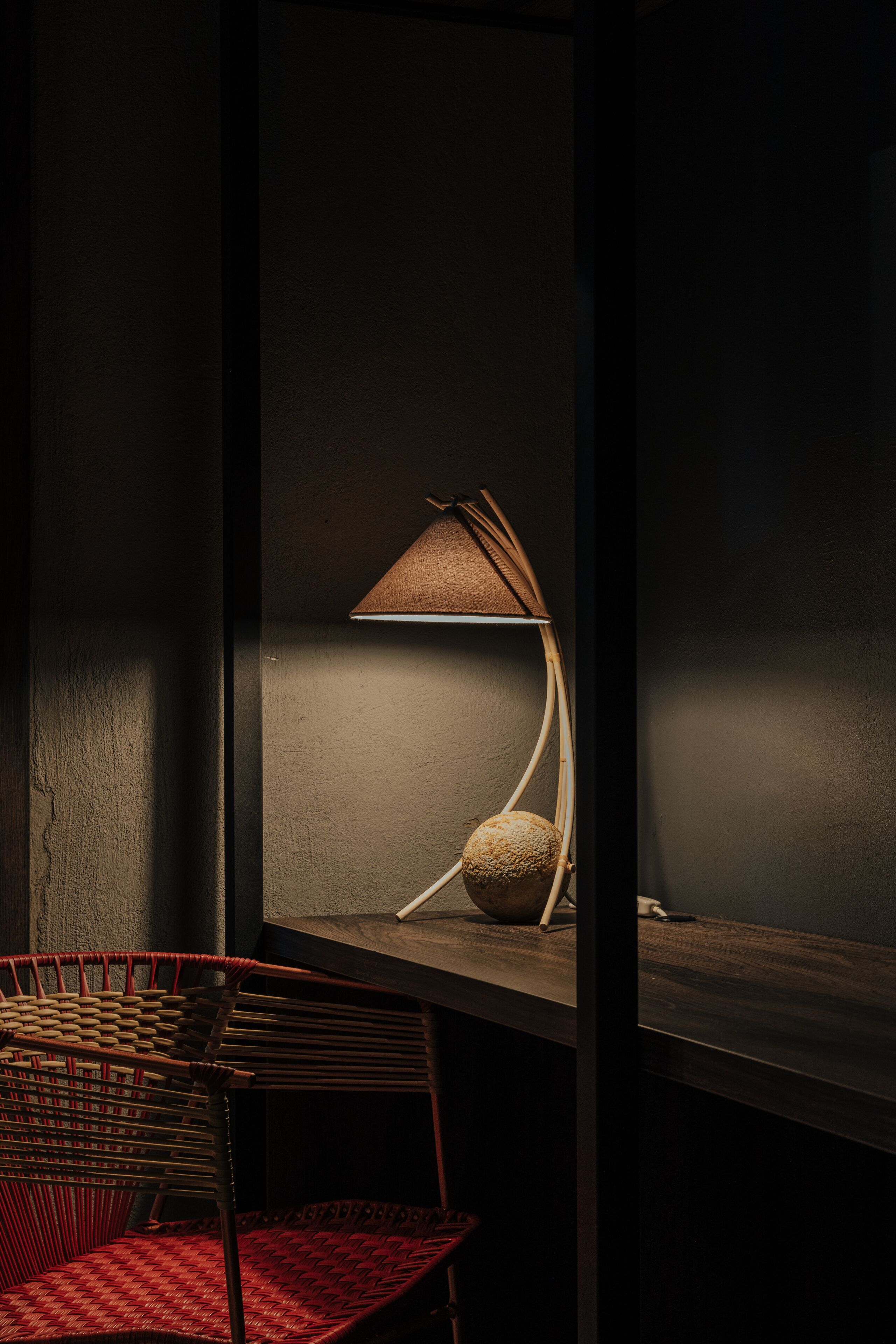 Una habitación oscura con una sola silla y una lámpara sobre una mesa.