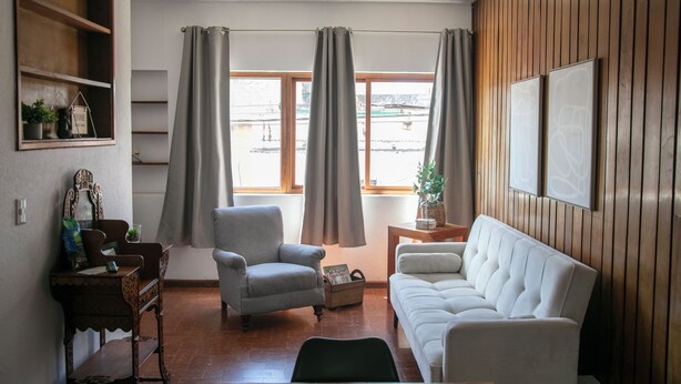 Ein Wohnzimmer mit einer Couch, einem Sessel, Holzregalen und einem kleinen Tisch.