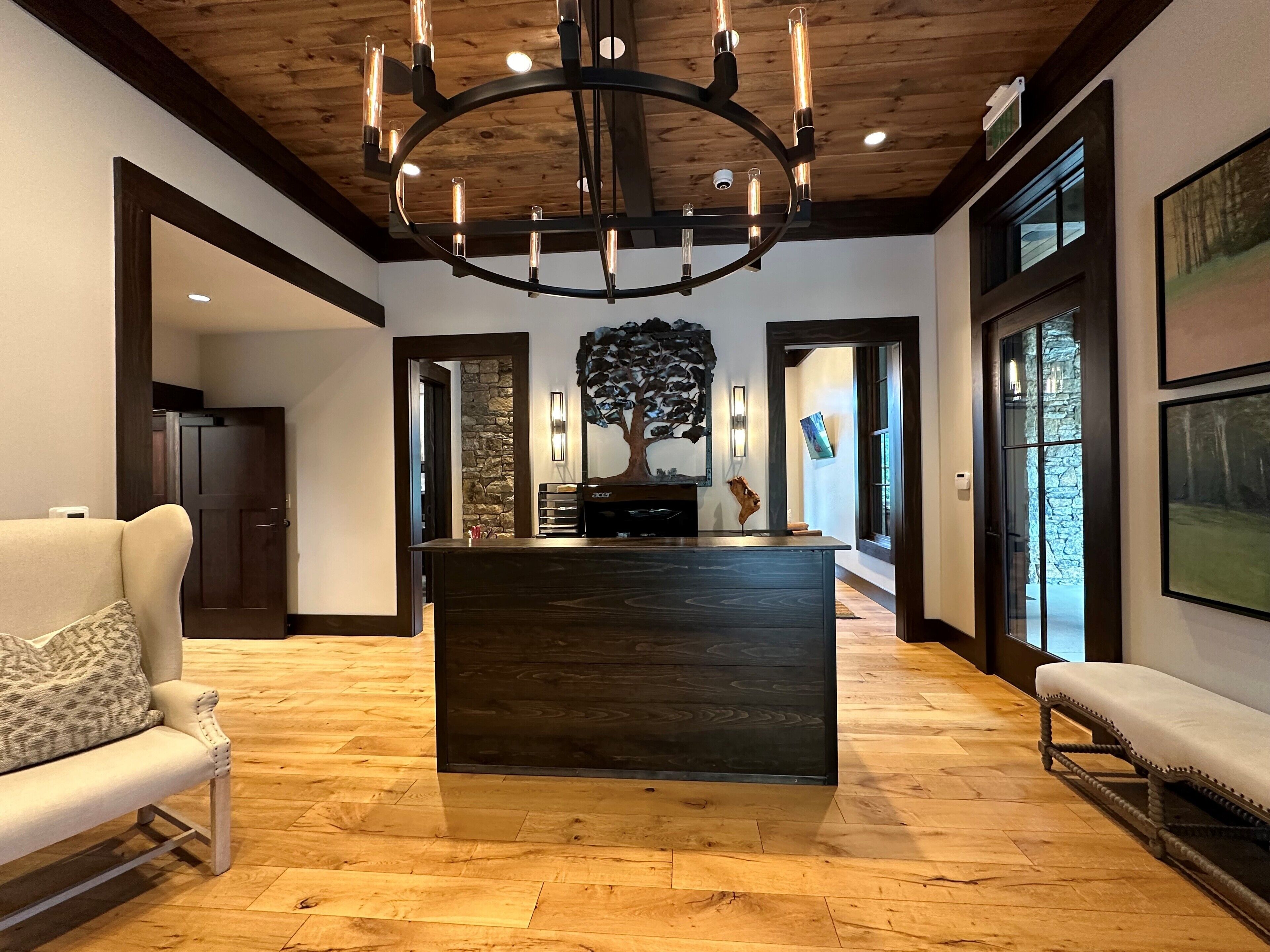 A spacious room with a wooden floor, a central dark wooden island, a white sofa, a bench, and a large chandelier.