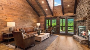 A cozy log cabin interior with a stone fireplace, wooden walls, and a large window overlooking a lush landscape. - Springdale Resort (Canton)