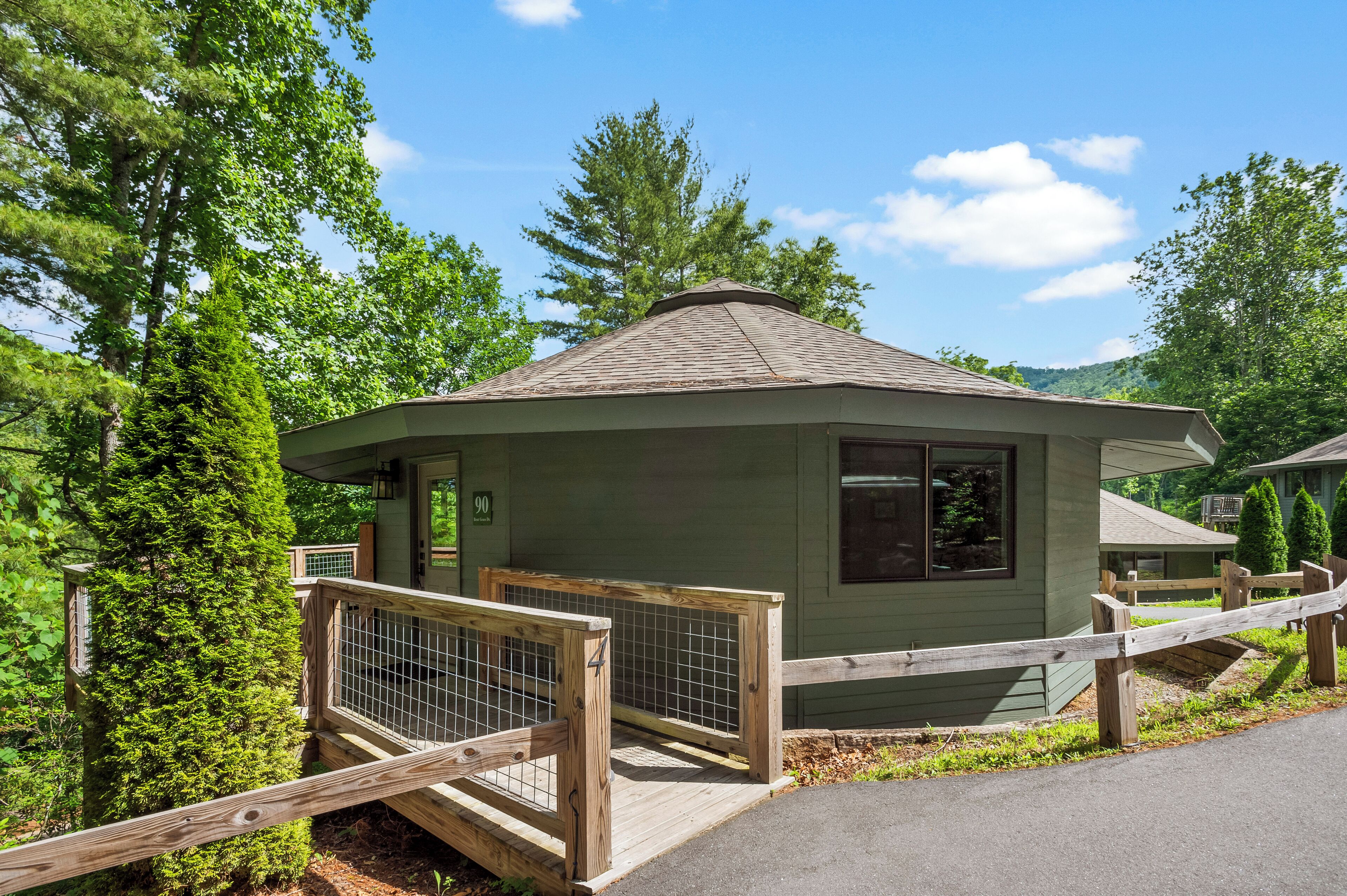 A small, single-story cabin with a fenced deck, surrounded by trees.