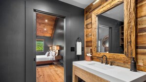 A modern bathroom with a wooden vanity, a large mirror, and a view into a bedroom with a bed and a window. - Springdale Resort (Canton)