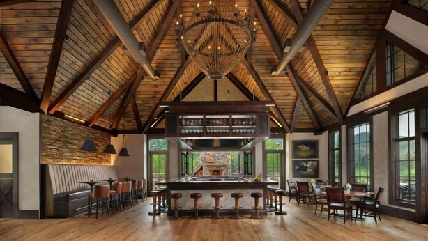 A spacious bar area with a high ceiling and exposed wooden beams, featuring a central bar with stools and a chandelier. - Springdale Resort (Canton)