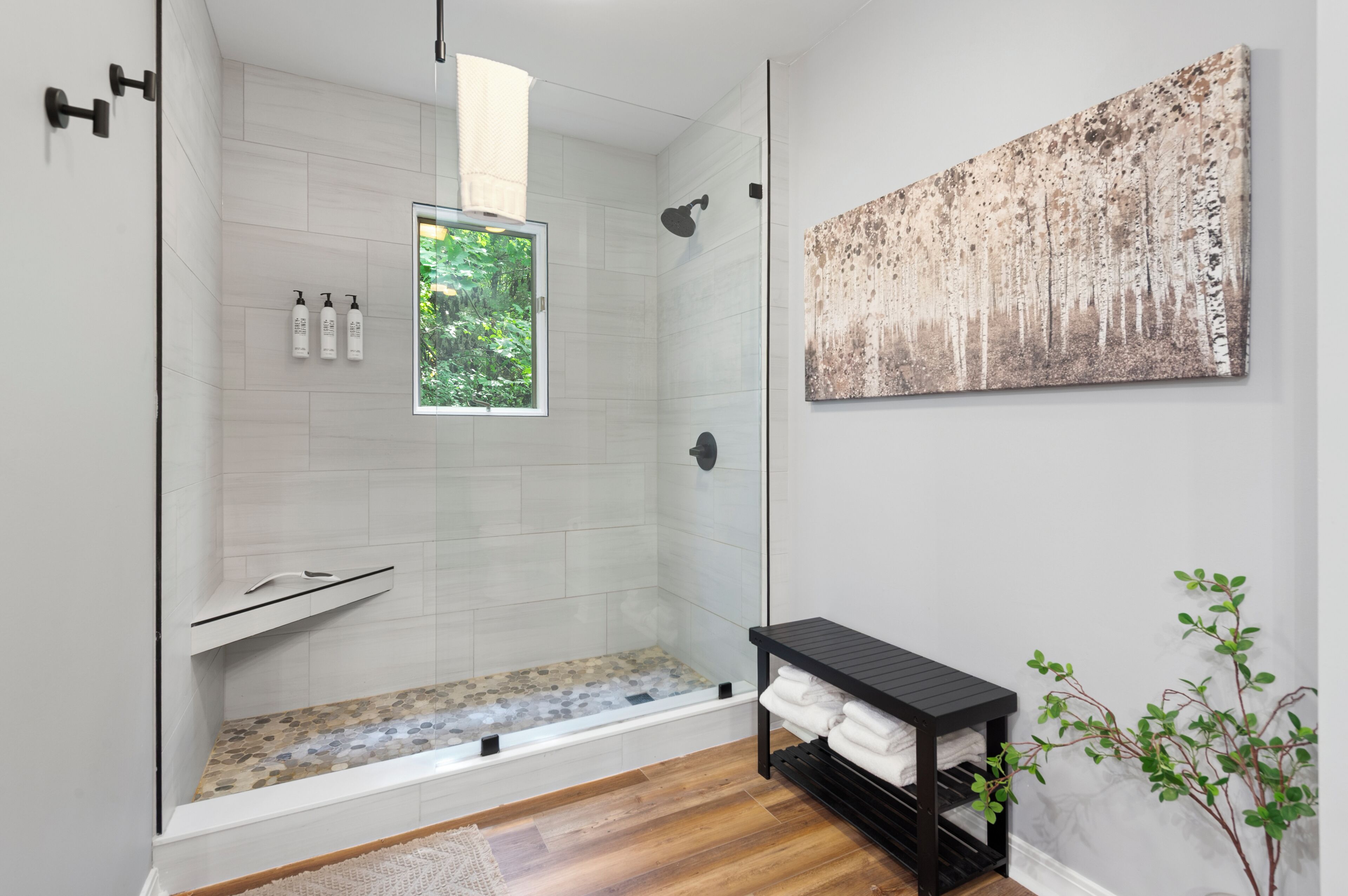 Une salle de bain moderne dotée d’une douche à parois de verre, d’une étagère intégrée, d’une grande fenêtre et d’une œuvre d’art accrochée au mur.