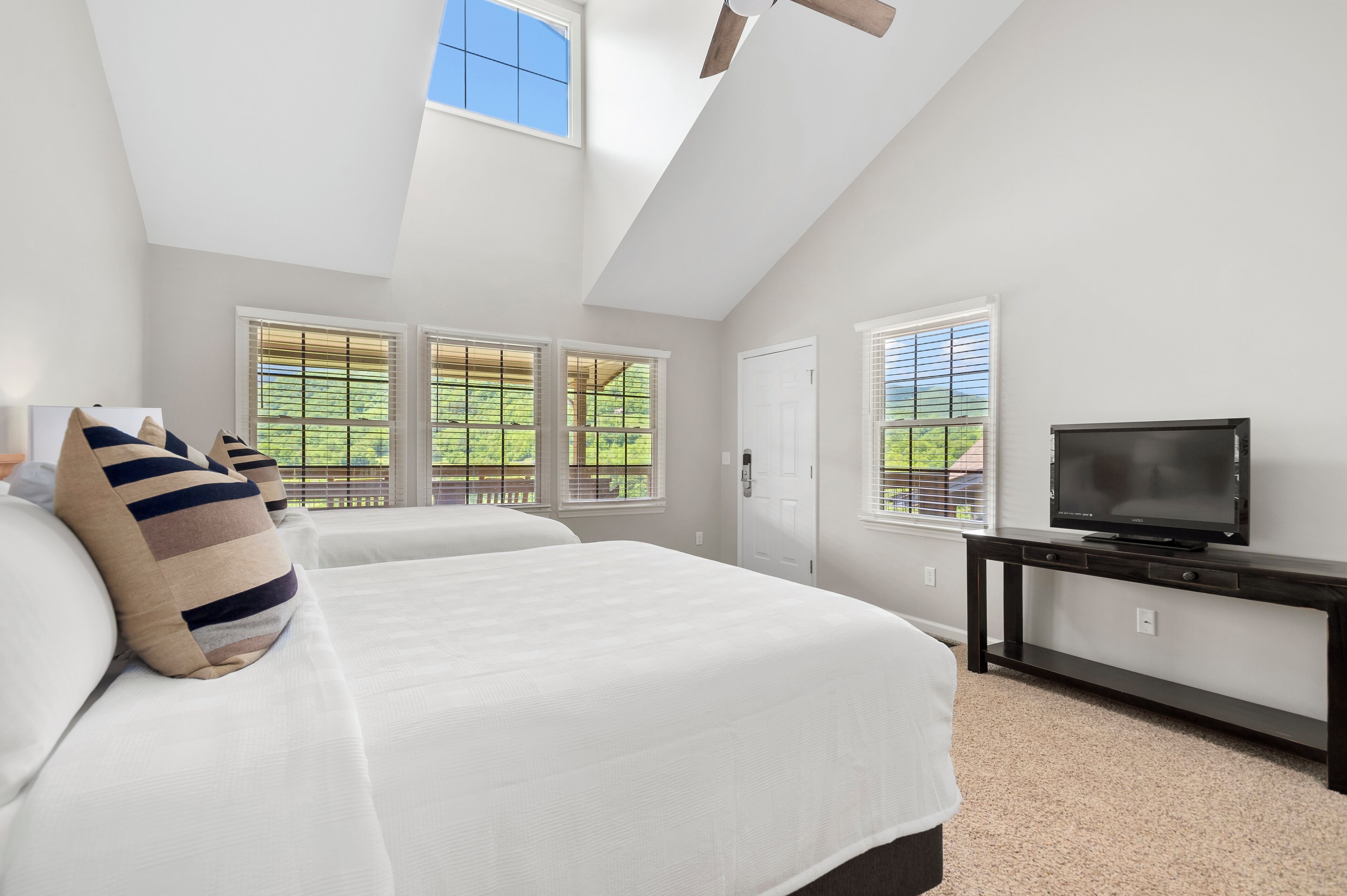 A bedroom with a large bed, a TV on a stand, and a skylight.
