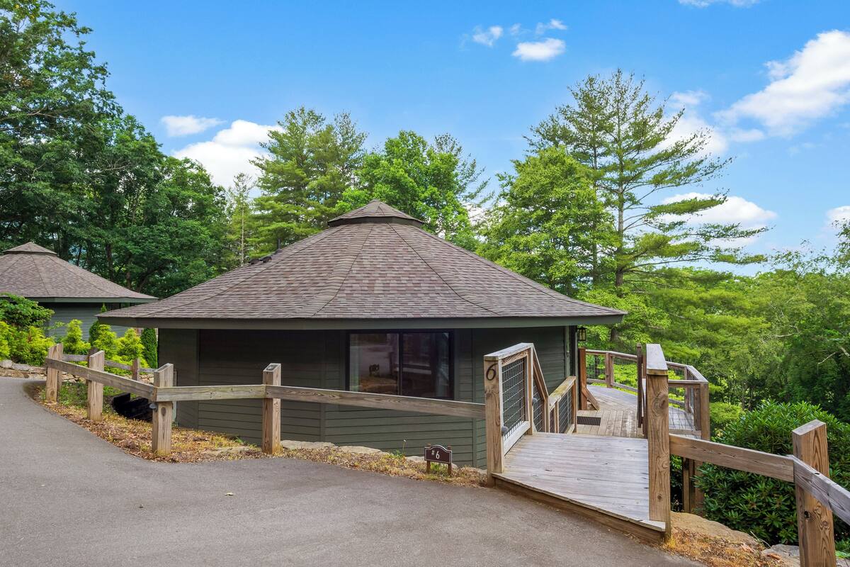 A small cabin with a wooden deck and a covered area, surrounded by dense greenery.