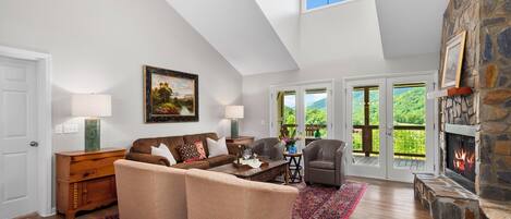 A spacious living room with a high ceiling, a stone fireplace, and a large window overlooking a scenic landscape.