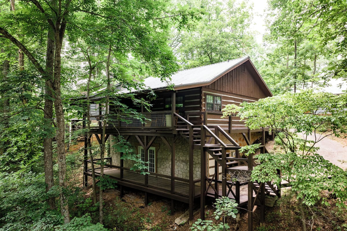 A wooden cabin with a stone foundation, surrounded by dense forest.