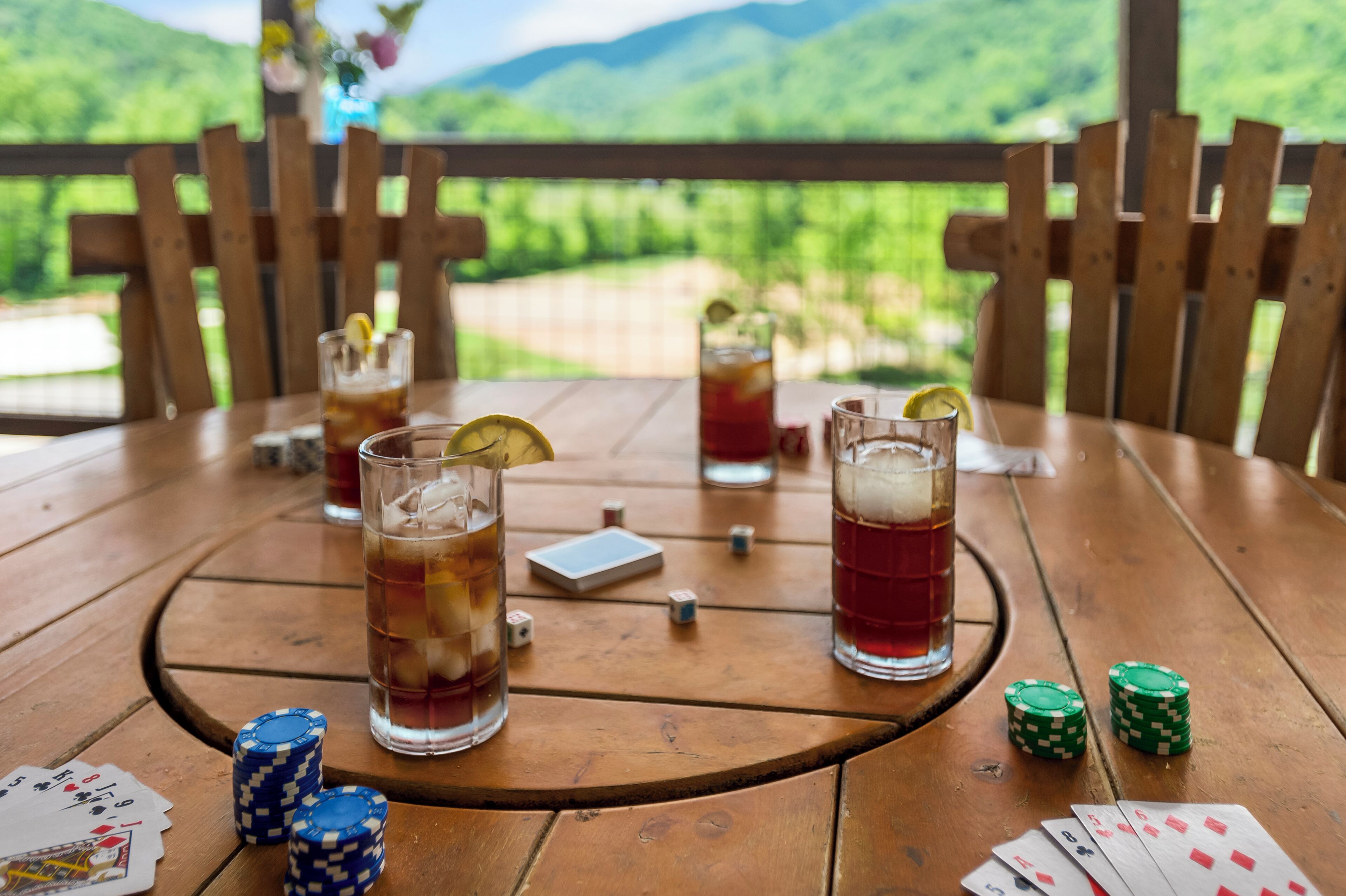 A wooden table with drinks, poker chips, and playing cards.