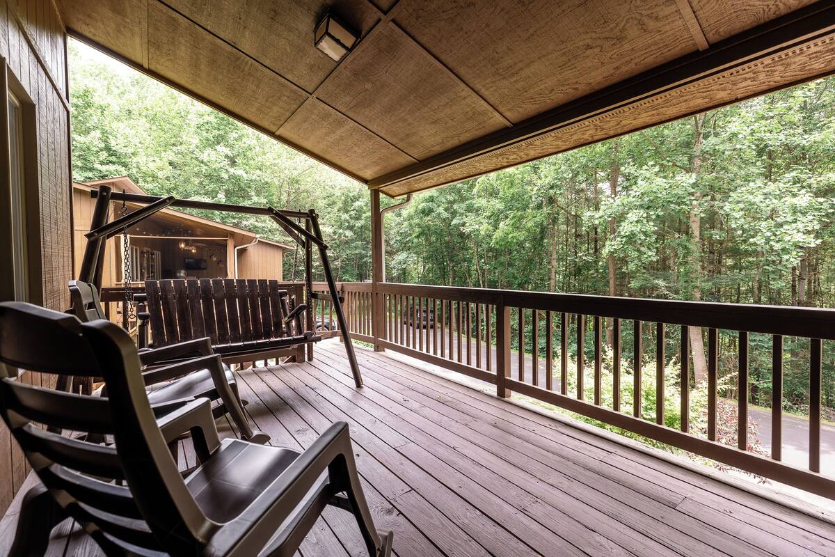 A wooden deck with a swing set and benches, overlooking a forested area.