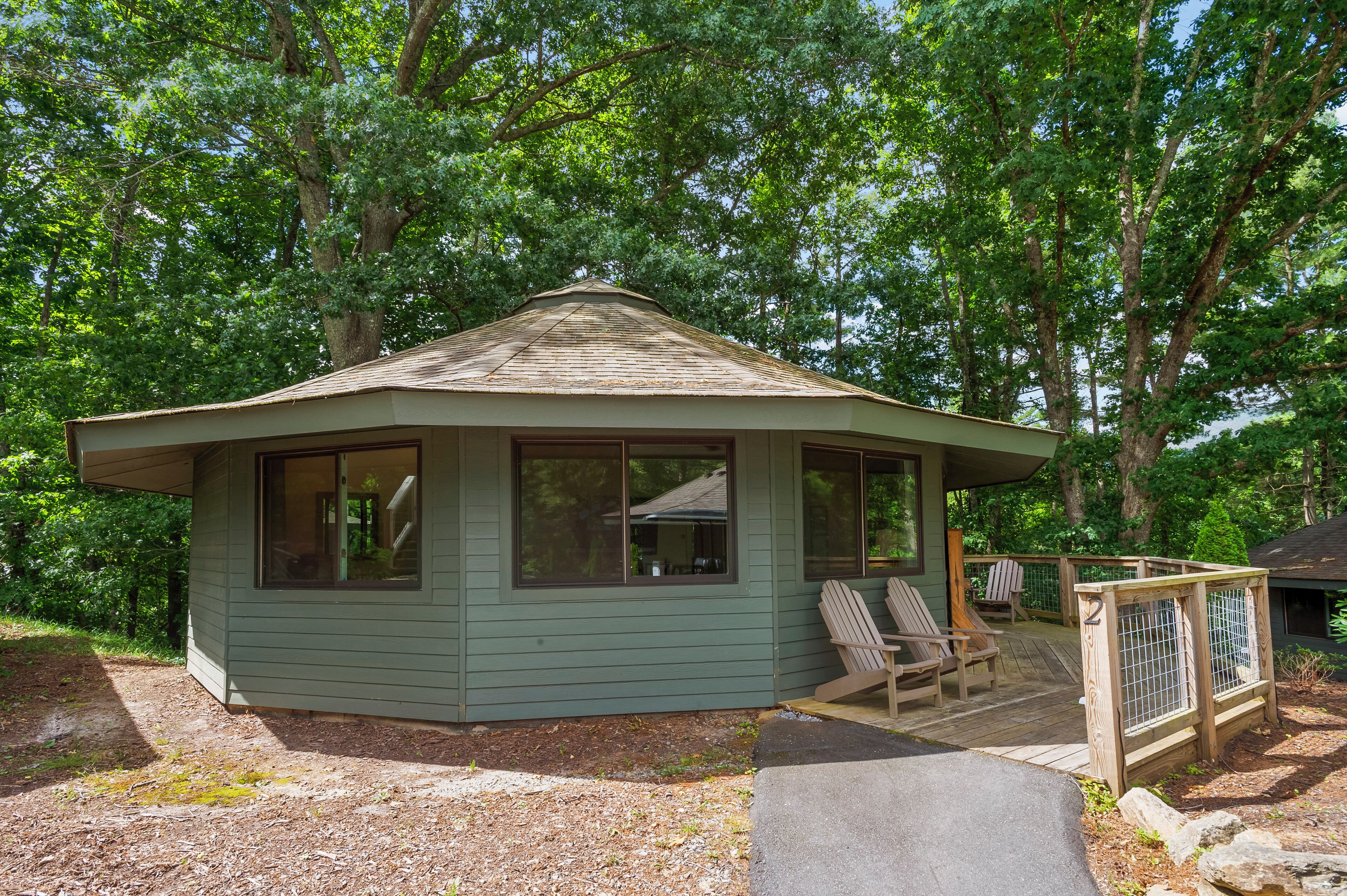A small, single-story cabin with a sloped roof, large windows, and a porch with two Adirondack chairs.