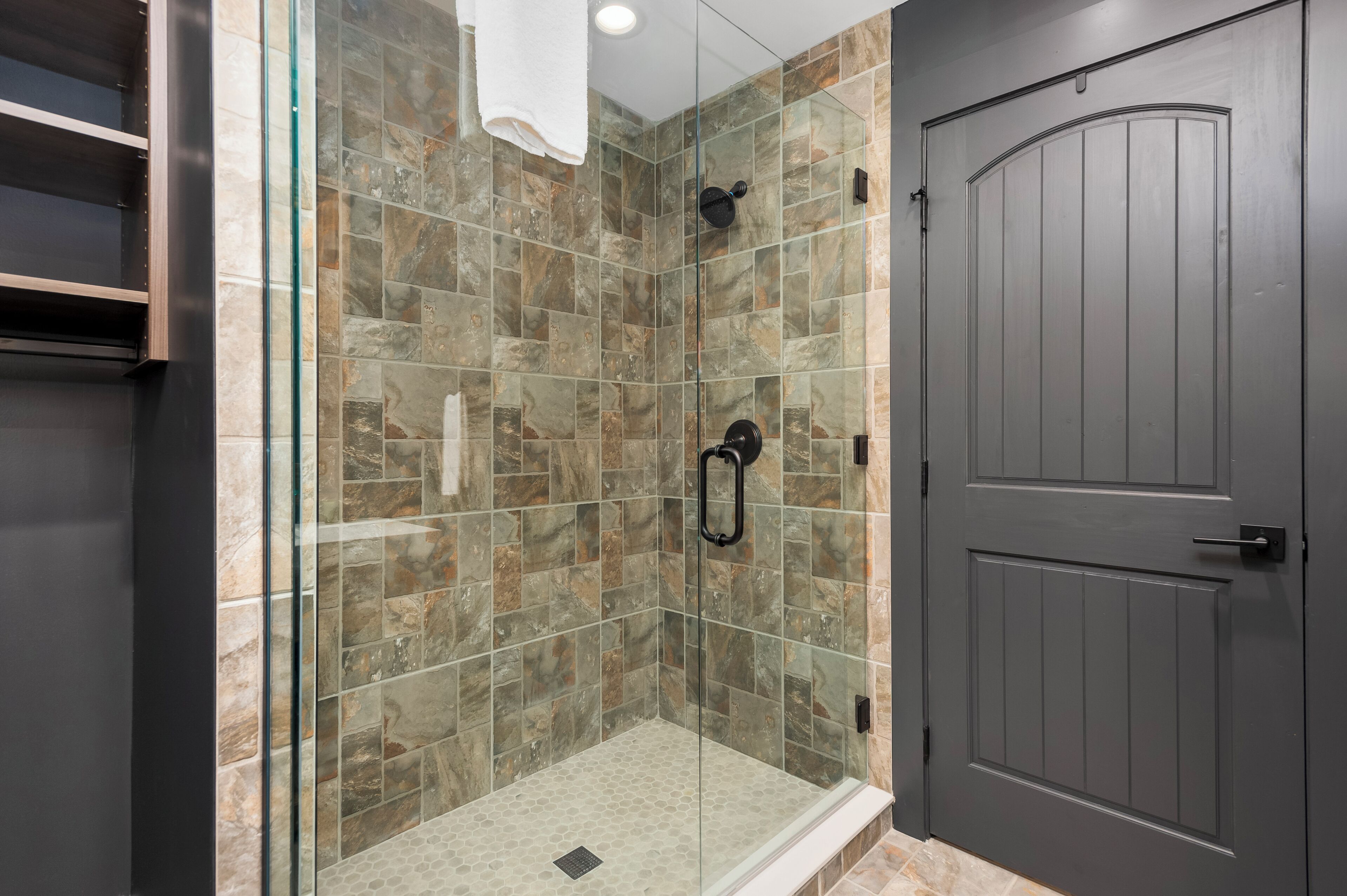 Un baño moderno con cabina de ducha de vidrio, baldosas de piedra y una puerta de madera oscura.