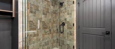 Un baño moderno con cabina de ducha de vidrio, baldosas de piedra y una puerta de madera oscura.