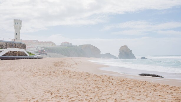 Une plage avec un phare, des affleurements rocheux et un ciel dégagé.