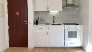 Une cuisine compacte avec des meubles blancs, un évier en acier inoxydable, un four encastré et une porte en bois.
