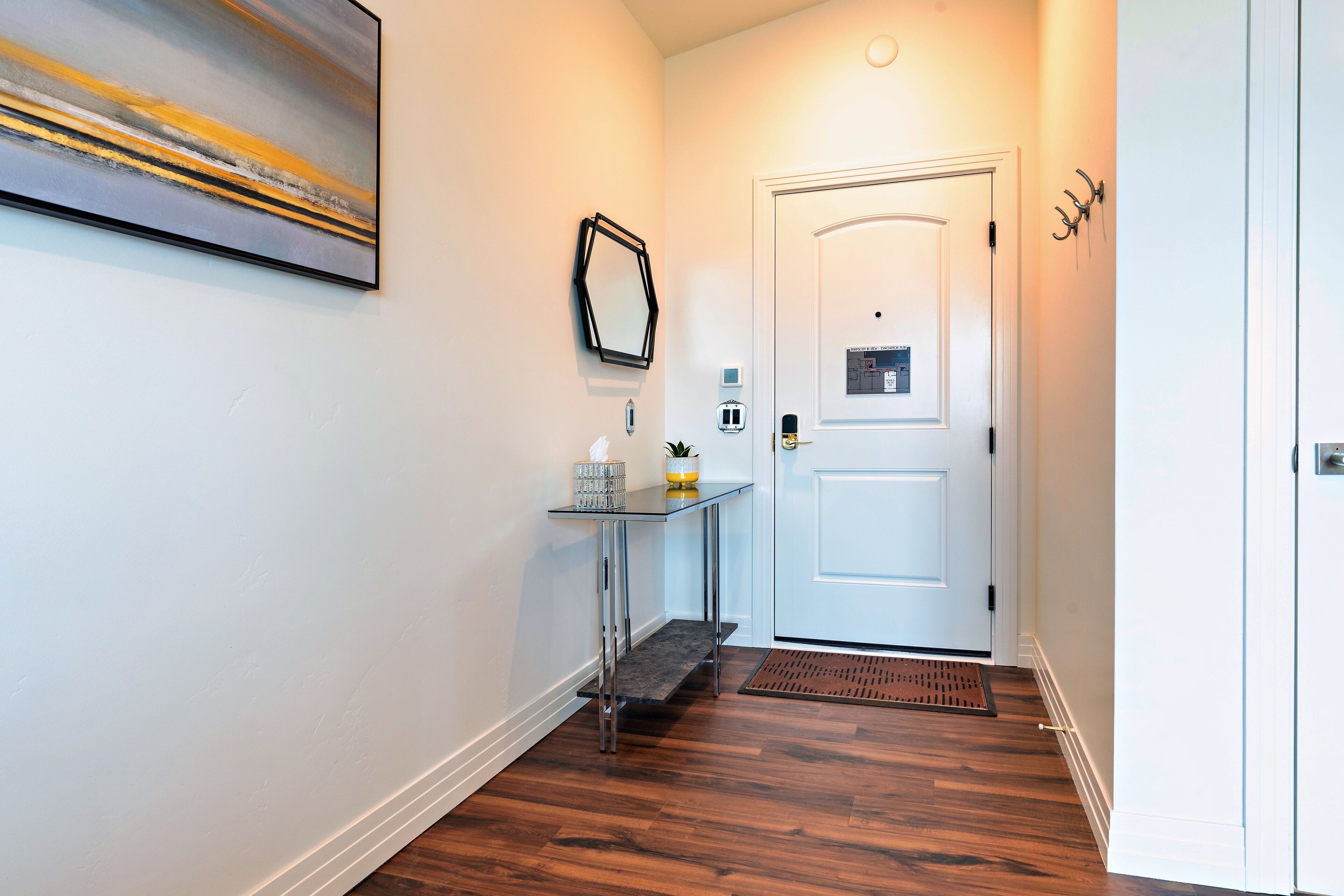 A hallway with a white door, a small table with a vase and a candle, and a painting on the wall.