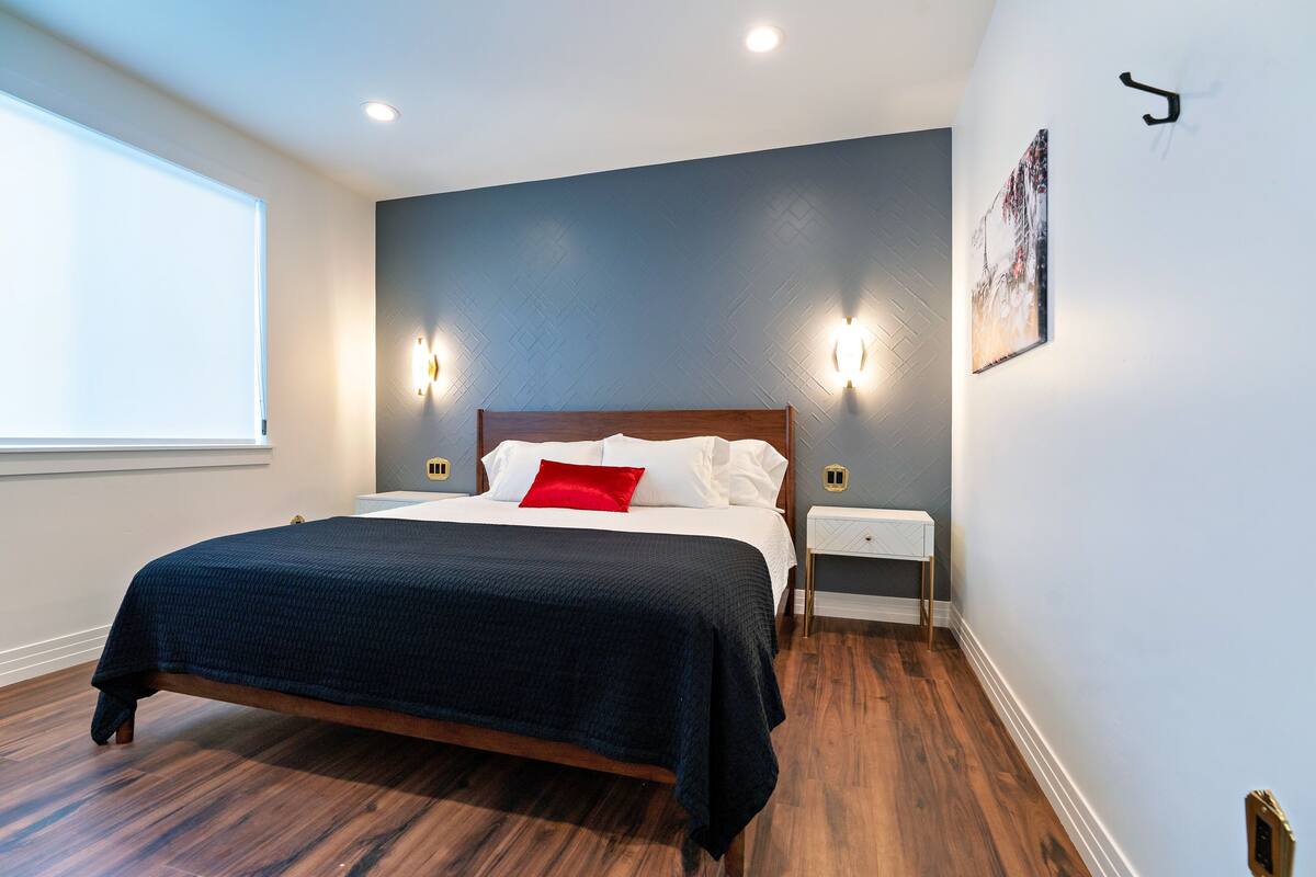 A bedroom with a bed, nightstands, a window, and wall-mounted lights.