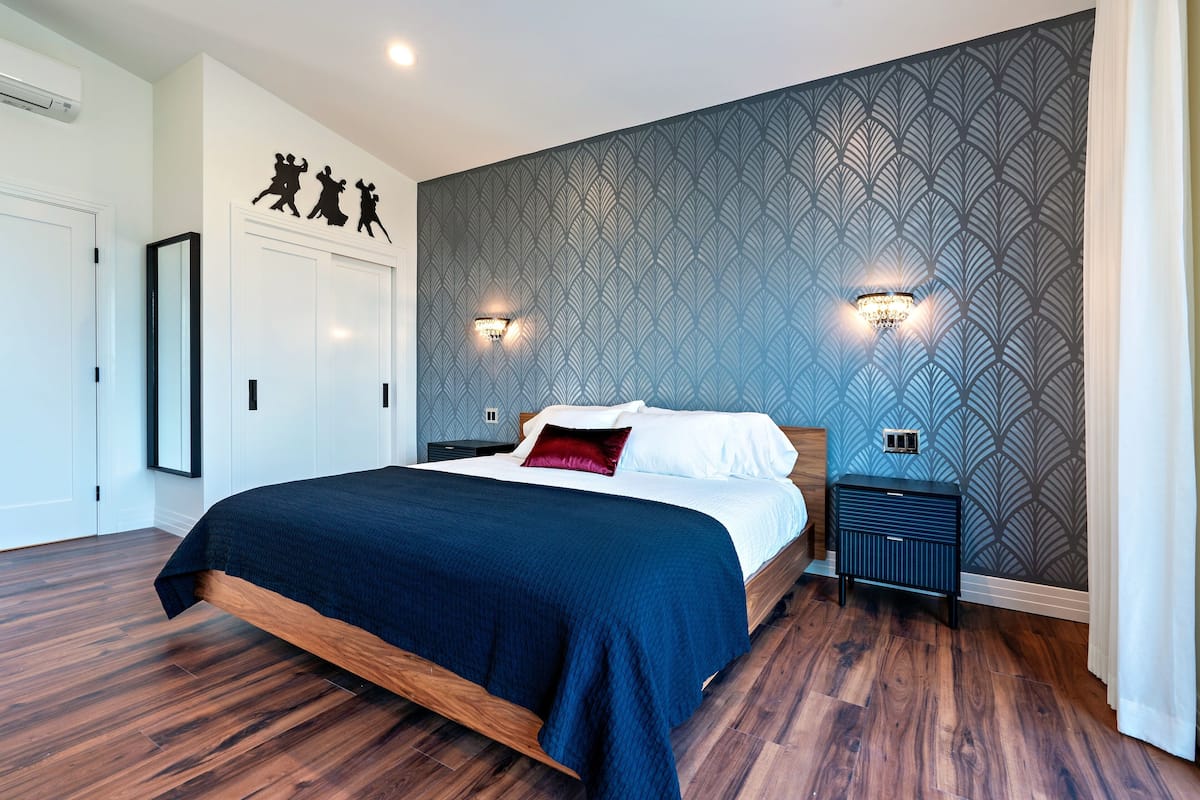 A modern bedroom with a wooden bed, dark blue bedding, and patterned wallpaper.