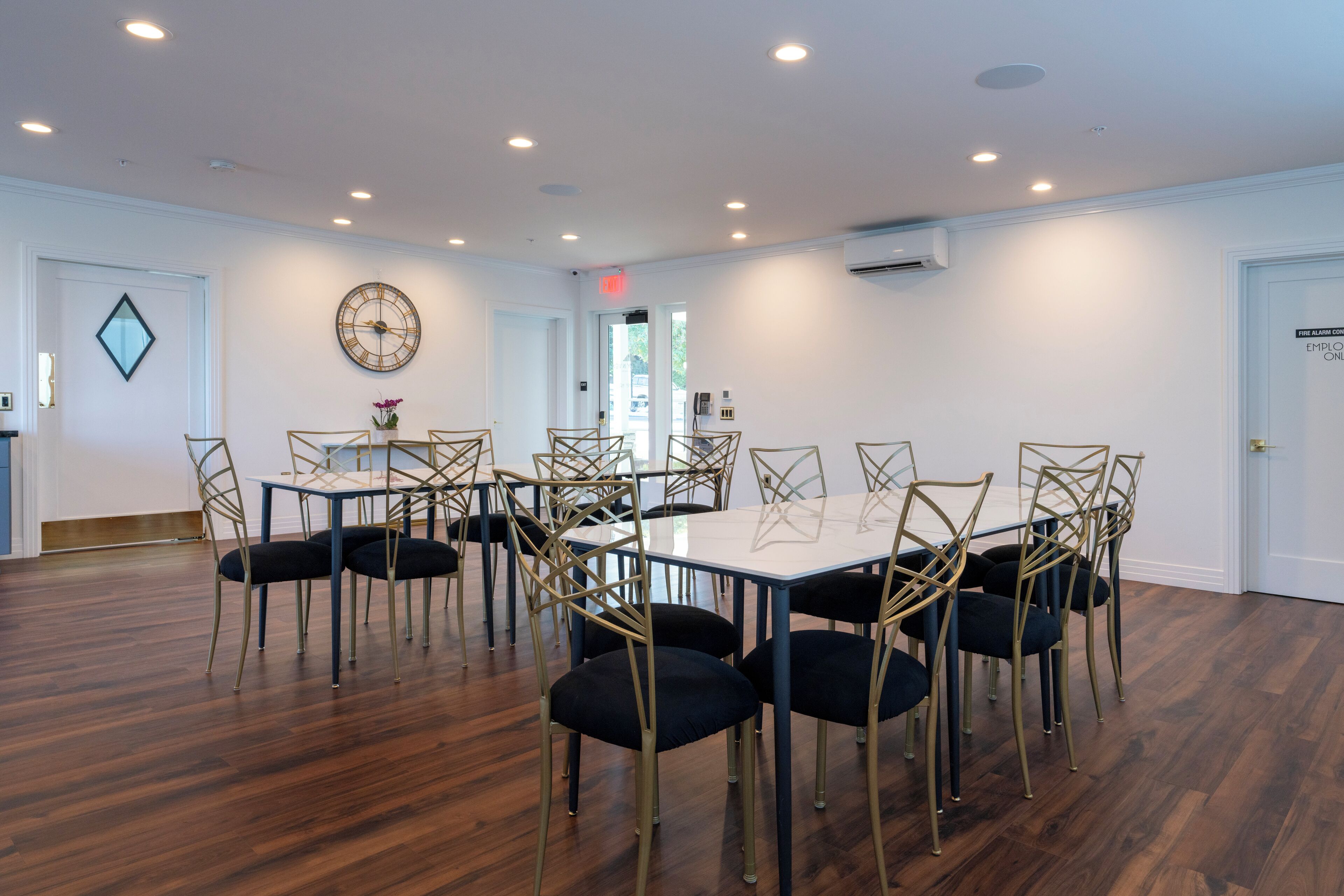 Uma sala de conferências com uma mesa retangular rodeada de cadeiras, um relógio na parede e um aparelho de ar condicionado.