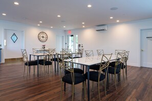 A conference room with a rectangular table surrounded by chairs, a clock on the wall, and an air conditioning unit.