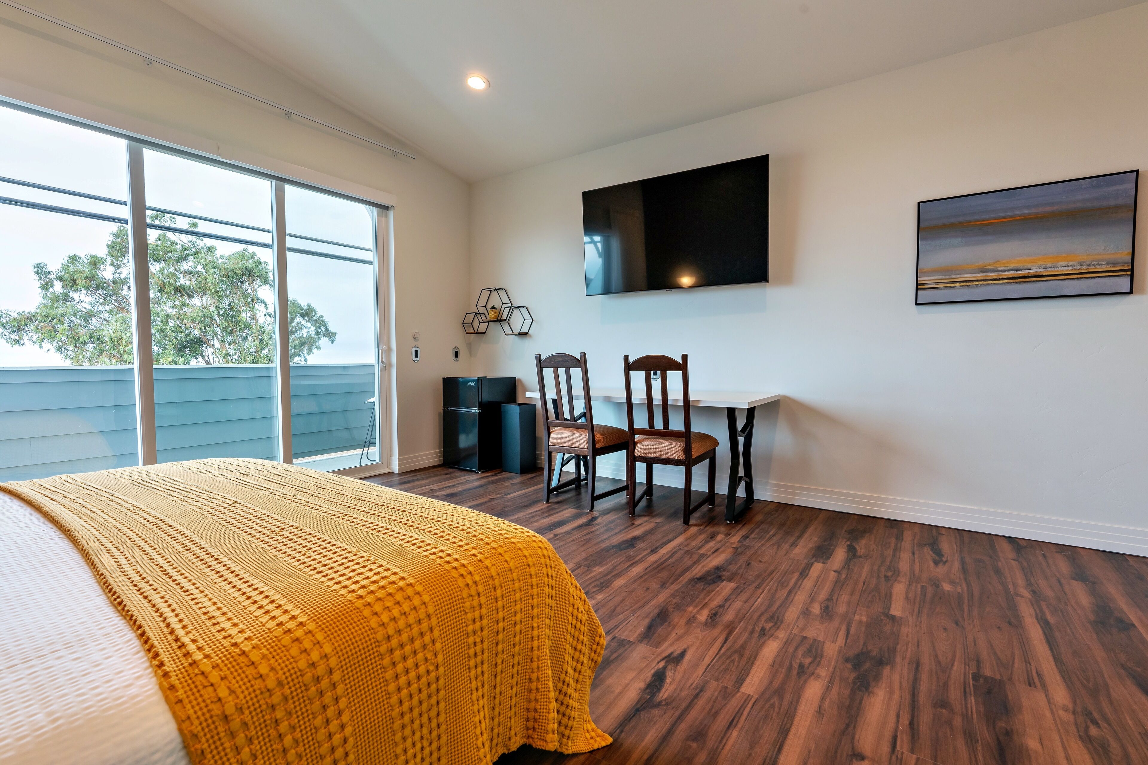 A bedroom with a large bed, a desk with two chairs, a flat-screen TV, and a painting on the wall.