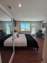 Un dormitorio moderno con una cama grande, un escritorio y dos sillas. Amplias ventanas con vistas al exterior.