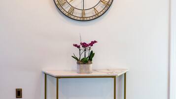 A wall-mounted clock with Roman numerals, a small table with a potted plant, and a white door.