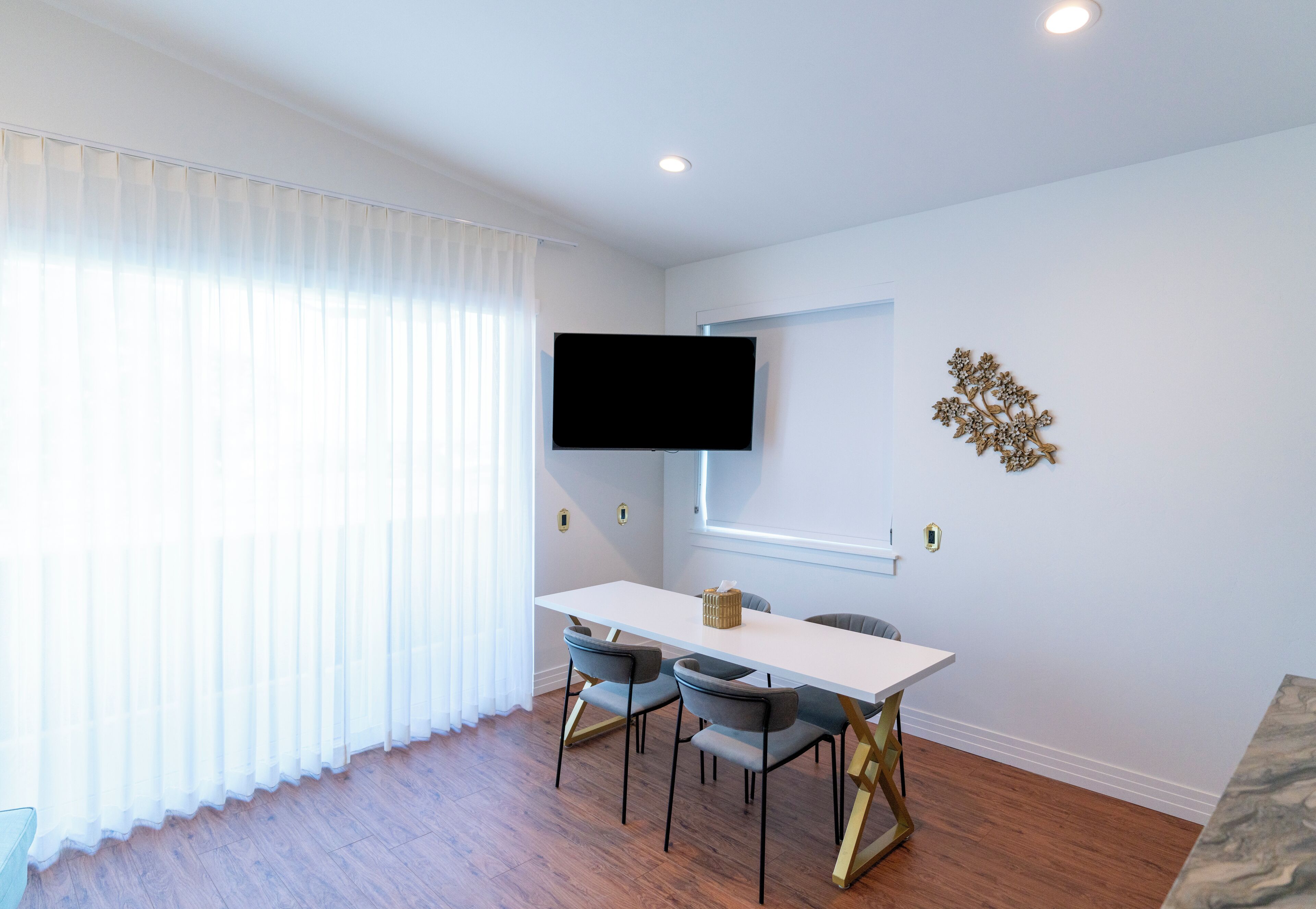 A modern dining area with a white table, four chairs, and a flat-screen TV mounted on the wall.