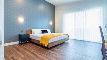 Un dormitorio con una cama grande, suelo de madera y una ventana con cortinas traslúcidas.