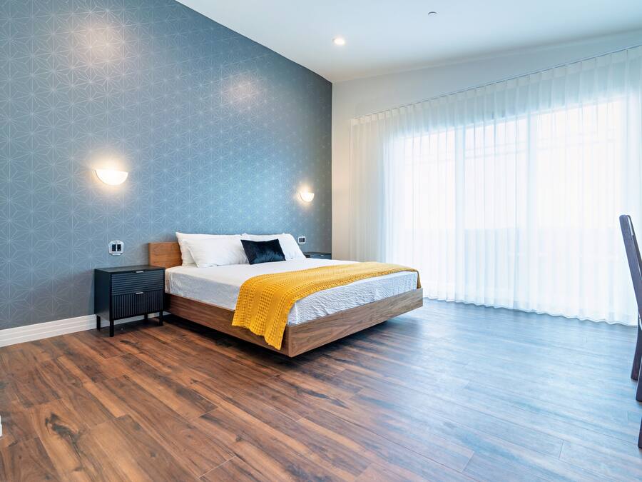Un dormitorio con una cama grande, suelo de madera y una ventana con cortinas traslúcidas.