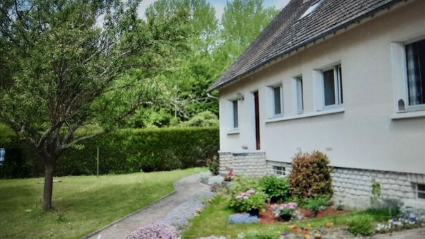 A two-story house with a white exterior and a stone foundation. There is a well-maintained lawn with a tree and a flower bed in the front yard. - Maison Lumineuse et Spacieuse en Forêt (Buthiers)