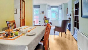 Une salle à manger avec une longue table dressée pour le repas, des chaises en bois et une vue sur le jardin par la fenêtre.