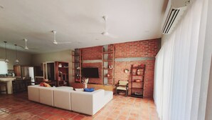 Ein geräumiges Wohnzimmer mit einem weißen Sofa, einem Fernseher und einer Ziegelwand.