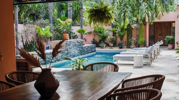 Ein Poolbereich mit Korbstühlen, einem Tisch mit einer Vase und Blick auf einen Pool und Grünflächen.