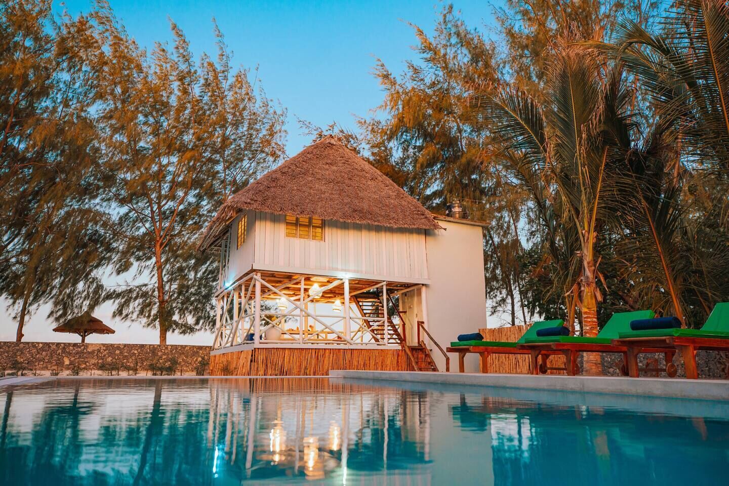 A poolside building with a thatched roof, surrounded by trees and a clear sky.