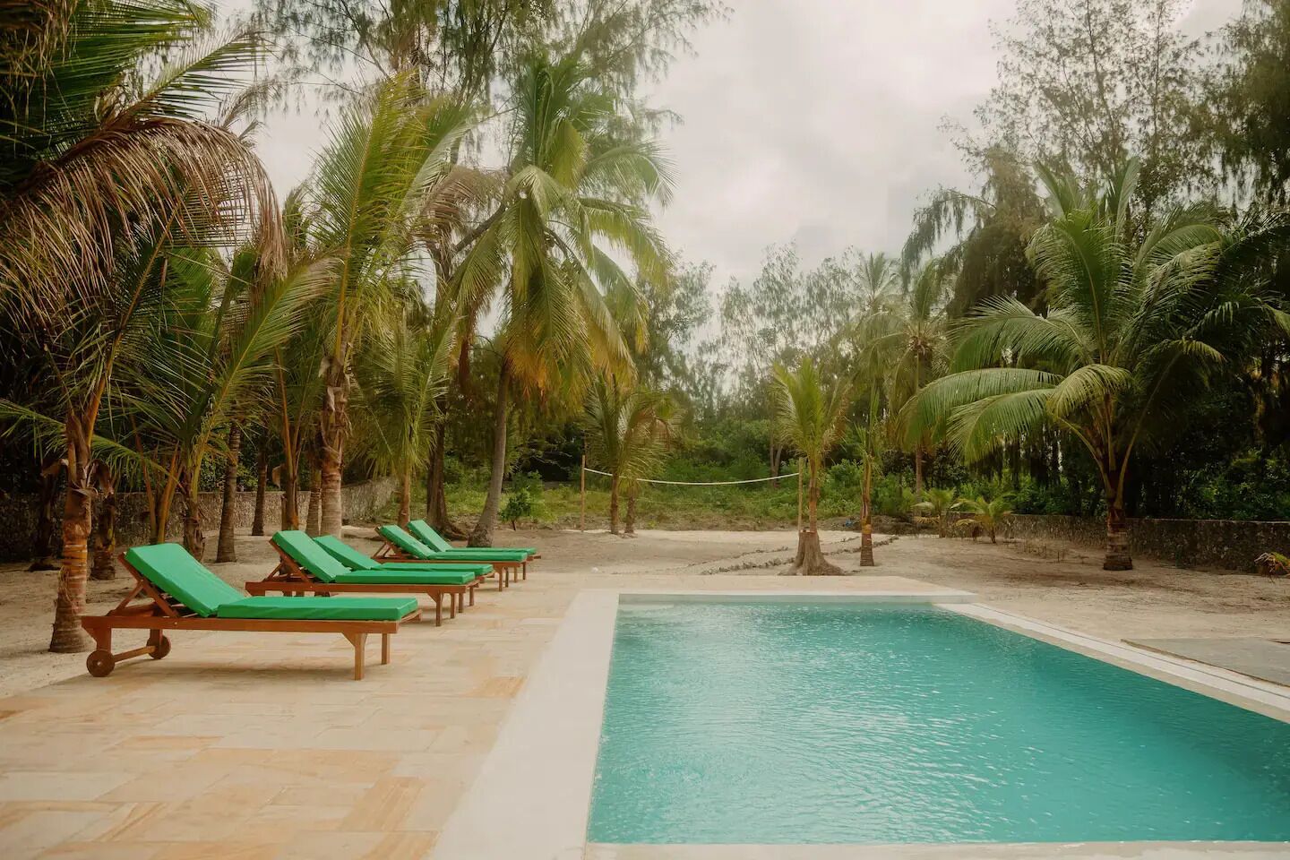 Un área de piscina con sillones de descanso y palmeras.