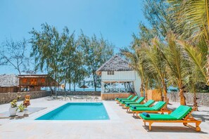 Un espace piscine avec des chaises longues, un petit bâtiment et des arbres.