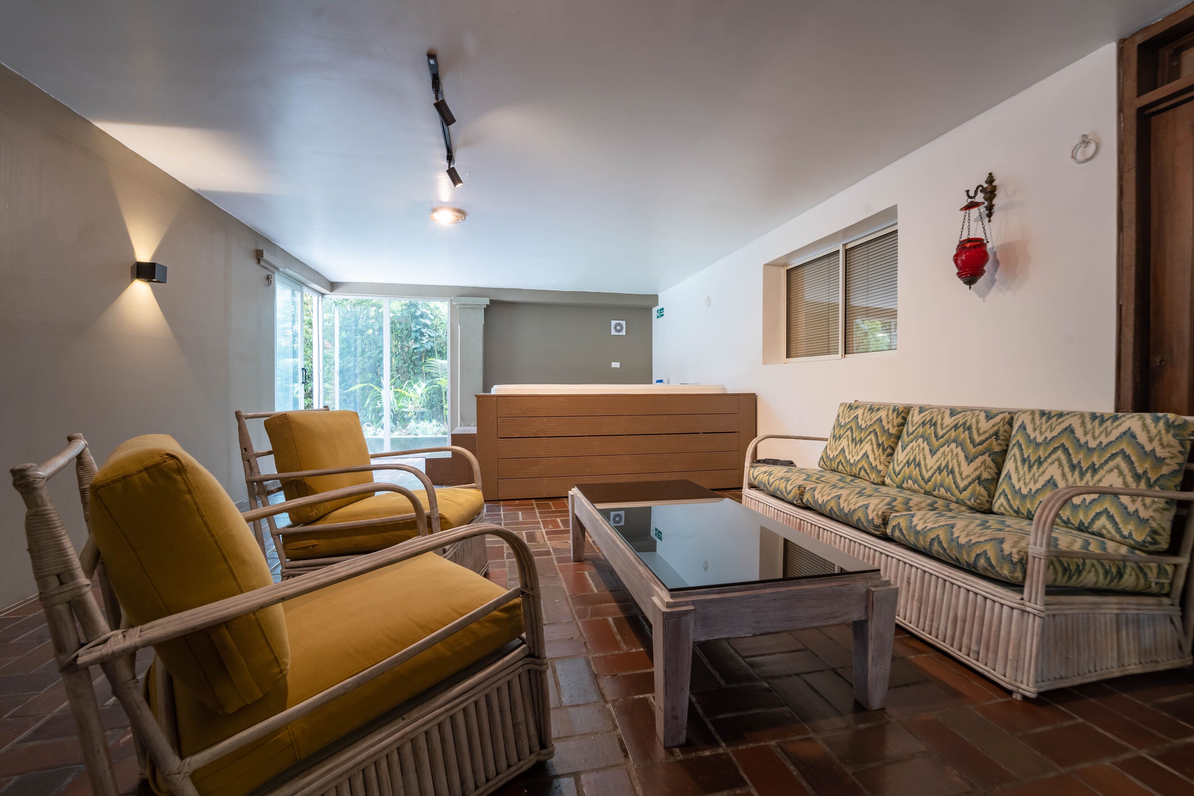 A living room with wicker furniture, a glass coffee table, and a sofa with patterned cushions.