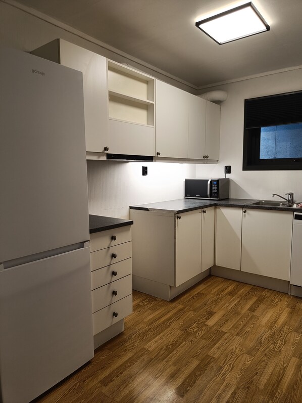 A modern kitchen with white cabinetry, a built-in microwave, and a window with blinds.