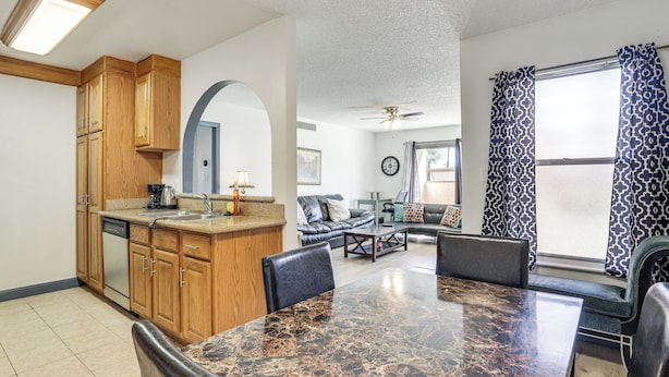 A kitchen with wooden cabinets, a dining table with chairs, a sofa, and a large window with patterned curtains. - WFH-Friendly Las Vegas Condo: 2 Mi to Strip! (Las Vegas)